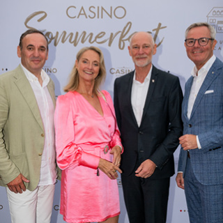 Drei Herren und eine Dame vor der Fotowand des Casino Konstanz Sommerfests lächeln in die Kamera.