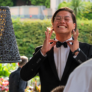 Ein glücklicher Croupier hält sich mit beiden Händen an die Fliege und grinst breit.